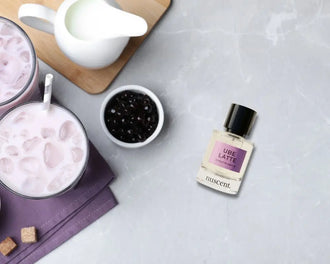 nuscent Ube Latte perfume bottle next to iced purple ube latte drinks and bubble tea pearls on marble surface