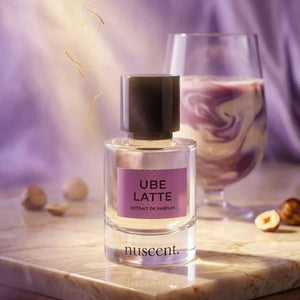 Ube Latte Extrait de Parfum bottle displayed on wooden surface with purple fabric backdrop and scattered hazelnut ingredients