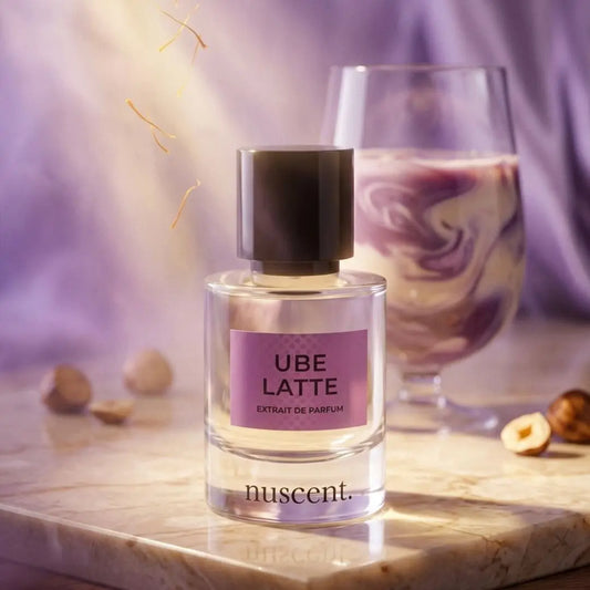 Ube Latte Extrait de Parfum bottle displayed on wooden surface with purple fabric backdrop and scattered hazelnut ingredients